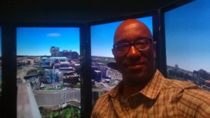 Coates in front of the liquid galaxy, a panoramic view of the earth based off the Earth code.  It's so large visitors actually feel immersed in the scene.